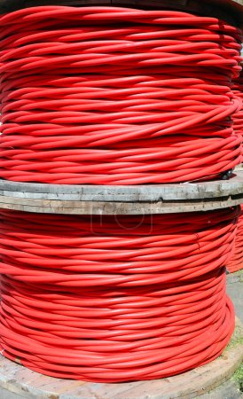 Photo for Two massive reels of thick red electrical power cable for transporting high voltage current with insulation for thousands of kVolts - Royalty Free Image
