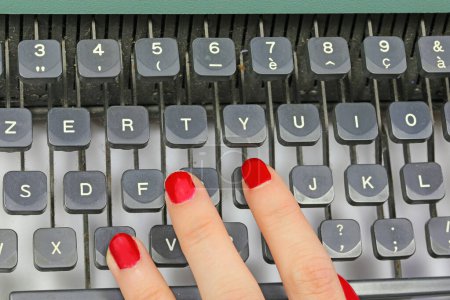 rote Nägel einer Sekretärin, die auf den Tasten einer alten Schreibmaschine in einem Büro tippt