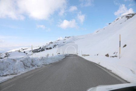 Téléchargez les photos : Route de montagne glissante glacée avec neige sur les côtés et poteaux pour marquer la limite de la chaussée vue de l'intérieur d'une voiture - en image libre de droit