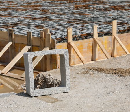 quadratisches Betonprodukt und Schalung aus gelben Holzbohlen während der Verlegung von Zement, um das Fundament des Gebäudes auf der Baustelle ohne Menschen zu machen