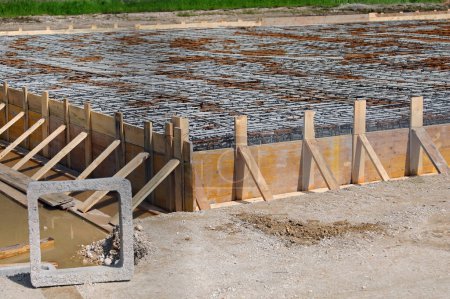 quadratisches Betonprodukt und Schalung mit gelben Bohlen während der Verlegung von Zement, um das Fundament des Gebäudes zu bilden