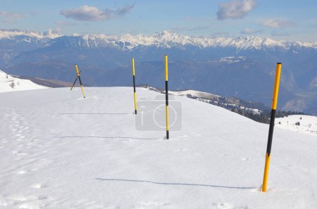 gelb und schwarz lackierte Stangen, die im Schnee stecken, um die Grenze der Schlucht in den Bergen im Winter abzugrenzen