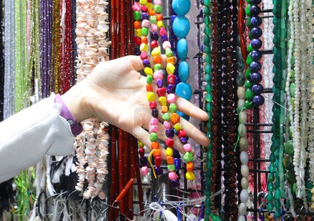 Hand eines jungen Mädchens, während sie sich für eine bunte Perlenkette im handgefertigten Accessoires-Ständer entscheidet