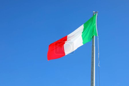 Large Italian flag with green, white, and red colors waving in the cloudless blue sky