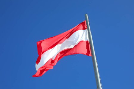 Österreichische Flagge in weiß-roten Farben weht vor wolkenlosem blauen Himmel