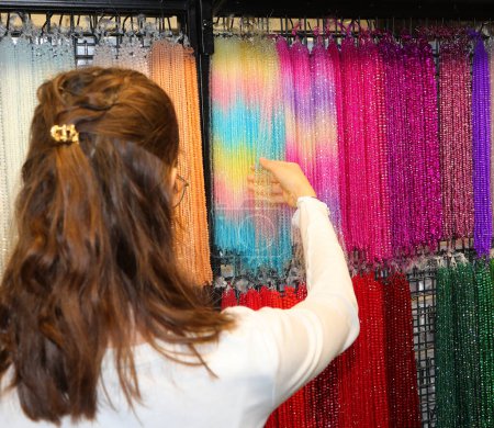 Mädchen bei der Auswahl einer roten Halskette aus Glasperlen unter vielen bunten Halsketten im Geschäft des Einkaufszentrums