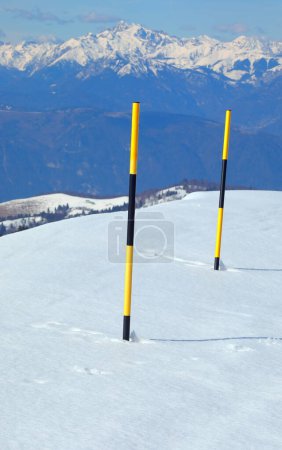 Hohe schwarz-gelbe Pfähle stecken im weißen Schnee, um im Winter die Schlucht in der Nähe der Straße in den Bergen abzugrenzen