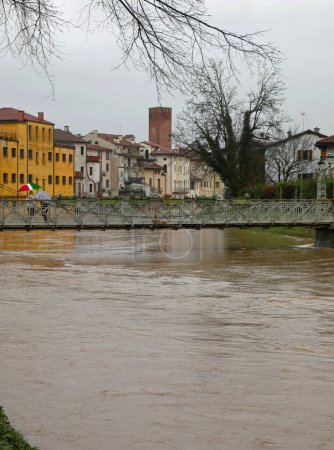 Stürmischer Fluss bei Überschwemmungen mit Überflutungsgefahr und fast überflutete Eiserne Fußgängerbrücke in Italien