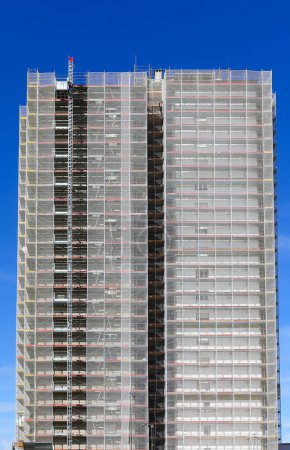 Riesiges Gerüst des gigantischen Wolkenkratzers während der Wartungsarbeiten zur Installation der Wärmedämmung für Energieeinsparung und blauen Himmel