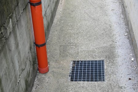 orange plastic gutter for collecting rainwater and the metal manhole cover of the inspectable drain in the concrete sidewalk