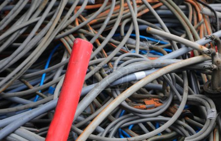 red electrical cord and many other tangled used electrical cords in landfill for recycling copper and polluting plastic
