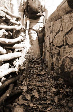 soldier with backpack and military uniform inside the narrow trench during the war in the front line of the battlefield