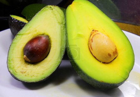 Two halves of an avocado with seeds and placed on a white plate
