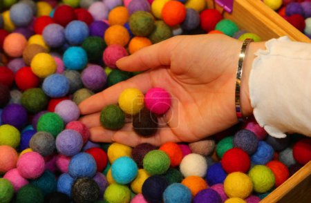 Foto de Mano de una joven sosteniendo bolas de colores hechos de lana hervida para crear un collar personalizado en la tienda de hobby - Imagen libre de derechos
