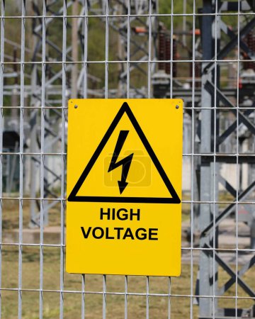 yellow sign with the big text high voltage with the triangle and the lightning outside the electrical substation