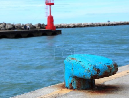 großer blauer Poller zum sicheren Anlegen von Schiffen im Hafen und ein roter Leuchtturm im Hintergrund