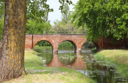 Ancient bridge made of red bricks with three arches over the river on the forest