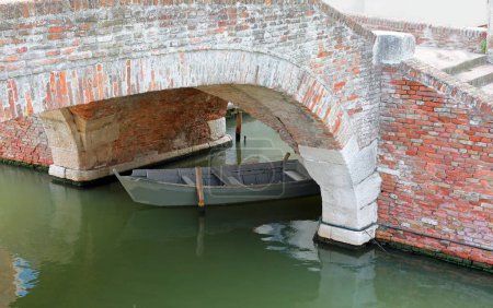 Antiguo puente de ladrillo de estilo veneciano con un barco debajo en un canal navegable