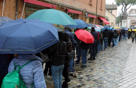 long line of people waiting their turn with umbrellas in the rain