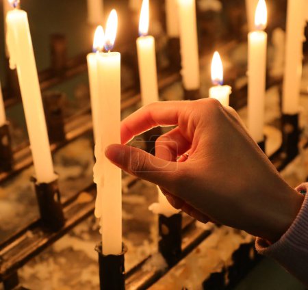Photo for Hand of girl lighting a votive candle in the holy place during the religious celebration of the faithful - Royalty Free Image