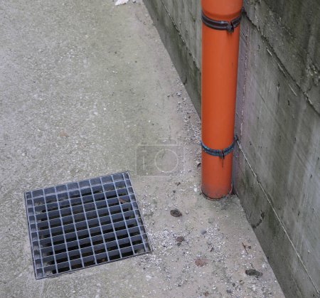 canalón para recoger el agua de lluvia y la cubierta metálica del desagüe inspeccionable en la acera de hormigón