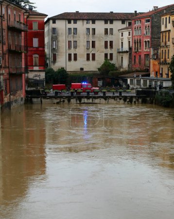 Fire truck with flashing blue siren on the bridge over the swollen river during the flood in the city