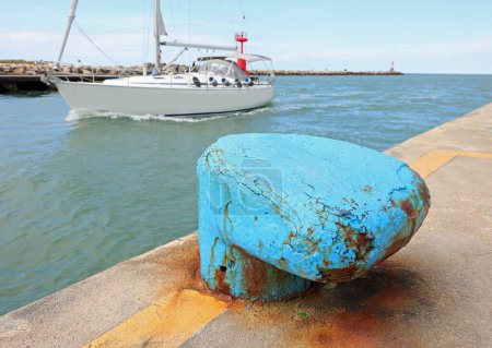 Gran pilona azul para amarre de barcos al muelle del puerto y un veloz barco navegando