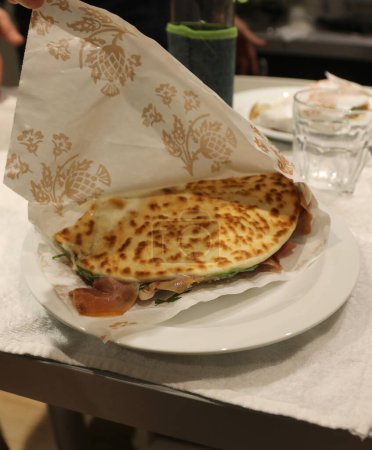 Typisch emilianische Küche ist die gefüllte Piadina, die auf einem Teller im Restaurant mit rohem Schinken und grünem Rucola gekocht wird