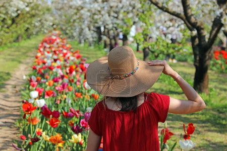 junges Mädchen mit Hand auf großem Strohhut inmitten des blühenden Feldes im Frühling