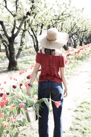 Mädchen mit Strohhut hält einen Eimer voller blühender Tulpen in hochauflösender Beleuchtung