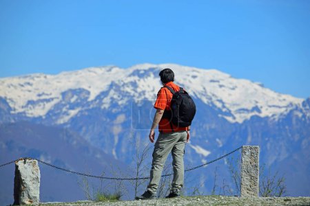 Hiker with black hair and backpack looking at snow-capped mountains in the distance