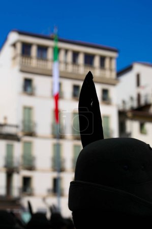 Black feather outline on Alpine hat and Italian flag in the background
