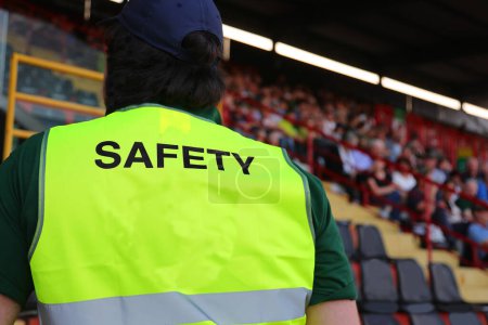 security guard wearing a uniform with the word SAFETY standing among the spectators in the stands during the event
