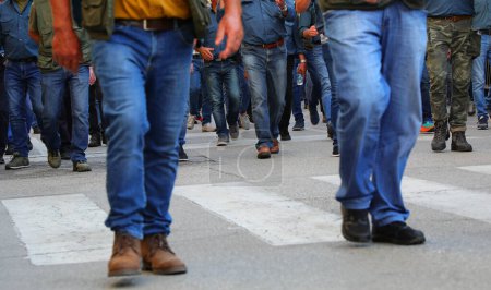legs of a crowd of men walking down the street in jeans and their faces cannot be seen