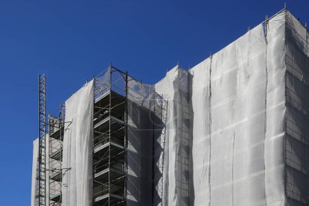 Construction scaffolding of a high-rise building with many apartments during the installation of insulation panels for energy consumption reduction
