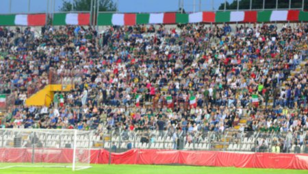 Intentionally blurred background of a large crowd of people in the packed stands of the stadium with tricolor flags and their faces are unrecognizable