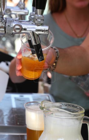 bartender pouring fresh lager beer from a tap into a glass at a pub with a waitres