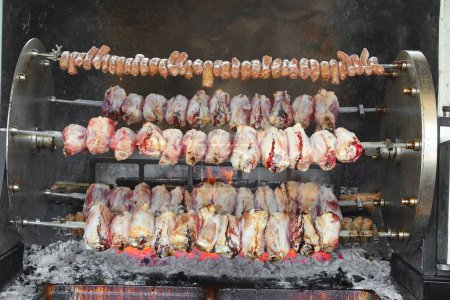 industrielle Grillserie mit Schweinefleisch und Würstchen, die über den offenen Flammen eines Restaurants im Freien kochen