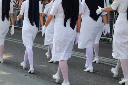 enfermeras con uniformes blancos bordeados marchando durante un desfile militar de la ciudad