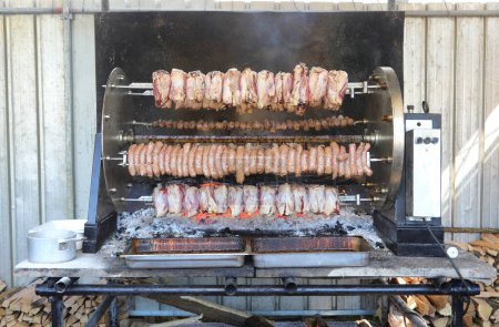 rotisserie laden with meat and sausage skewers, turning over glowing embers at the village fair