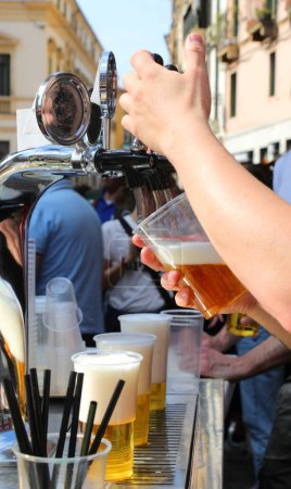 Barkeeper schüttet bei Outdoor-Party ein Plastikglas mit eiskaltem blonden Bier ein