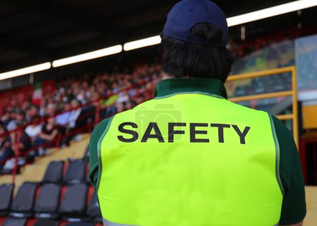 stadium steward with the phosphorescent jacket and the big SAFETY writing who controls the fans in the packed stands