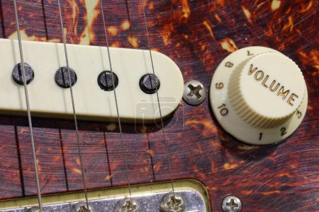 detail of the volume knob with the engraved text and the pickpu of the electric guitar with a wooden background