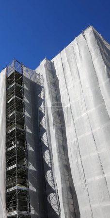 Baugerüst eines modernen Gebäudes mit vielen Wohnungen während der Installation von Isolierplatten zur Senkung des Energieverbrauchs