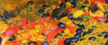Detail der Zutaten der valencianischen Fischpaella mit Reis-Paprika, grünen Erbsen Oliven Miesmuscheln, Weichtieren und roten Tomaten