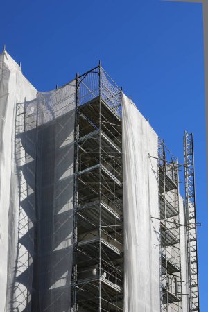 Large building with scaffolding during installation of insulation panels to save energy and gas and blue sky
