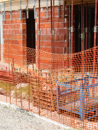 Baustelle für ein Gebäude, das von einem orangefarbenen Zaun umgeben ist, um unbefugten Zugang zum Arbeitsbereich zu verhindern