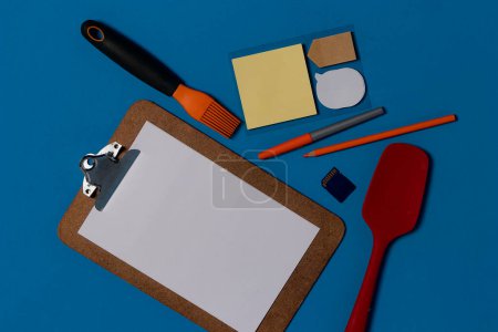 Photo for Chef's Culinary Workspace: Blue Table with Recipe Notepad, Kitchen Utensils, Papers, and Pen - Royalty Free Image