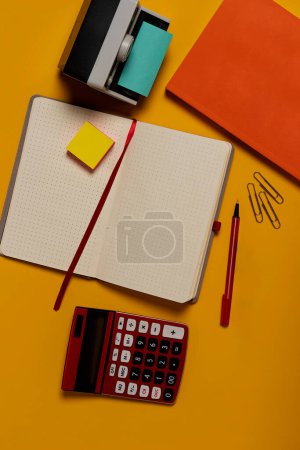 Photo for Photographer's Creative Workspace: Yellow Table with Blank Notebook, Calculator, Pens, Paper Clips for Idea Generation - Royalty Free Image