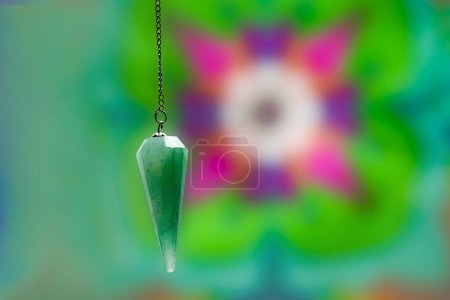 Photo for Turquoise pendulum used for divagation suspended in front of a colorful background - Royalty Free Image